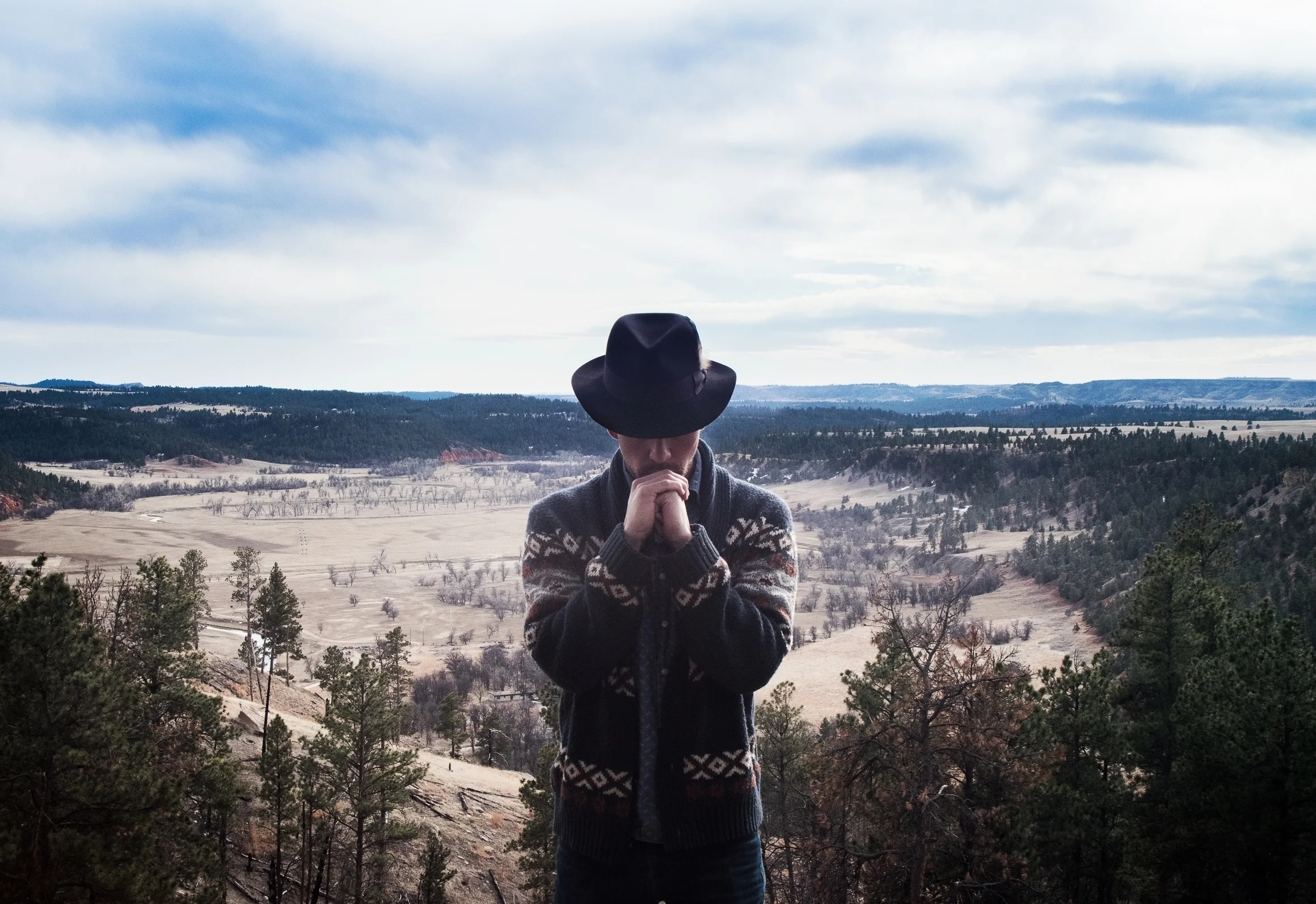 Shawn-Caulin Young in a cowboy hat, hands together, in a wide winter landscape